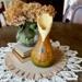 A vase made from a dried gourd. It is a brown to green ombre stain, with a iridescent butterfly wood burned on the front.  